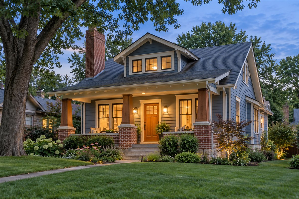 Craftsman bungalow with cedar porch columns, cream trim and a brick chimney at dusk