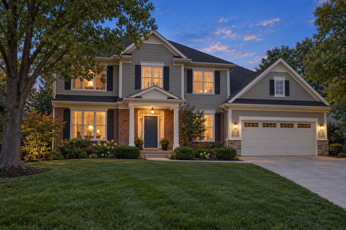 Warm-gray two-story home with brick accents and a navy front door at dusk