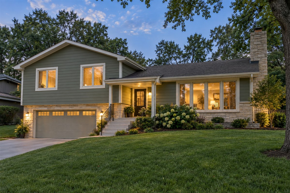 Sage-green split-level home with limestone accents and warm porch lights at dusk