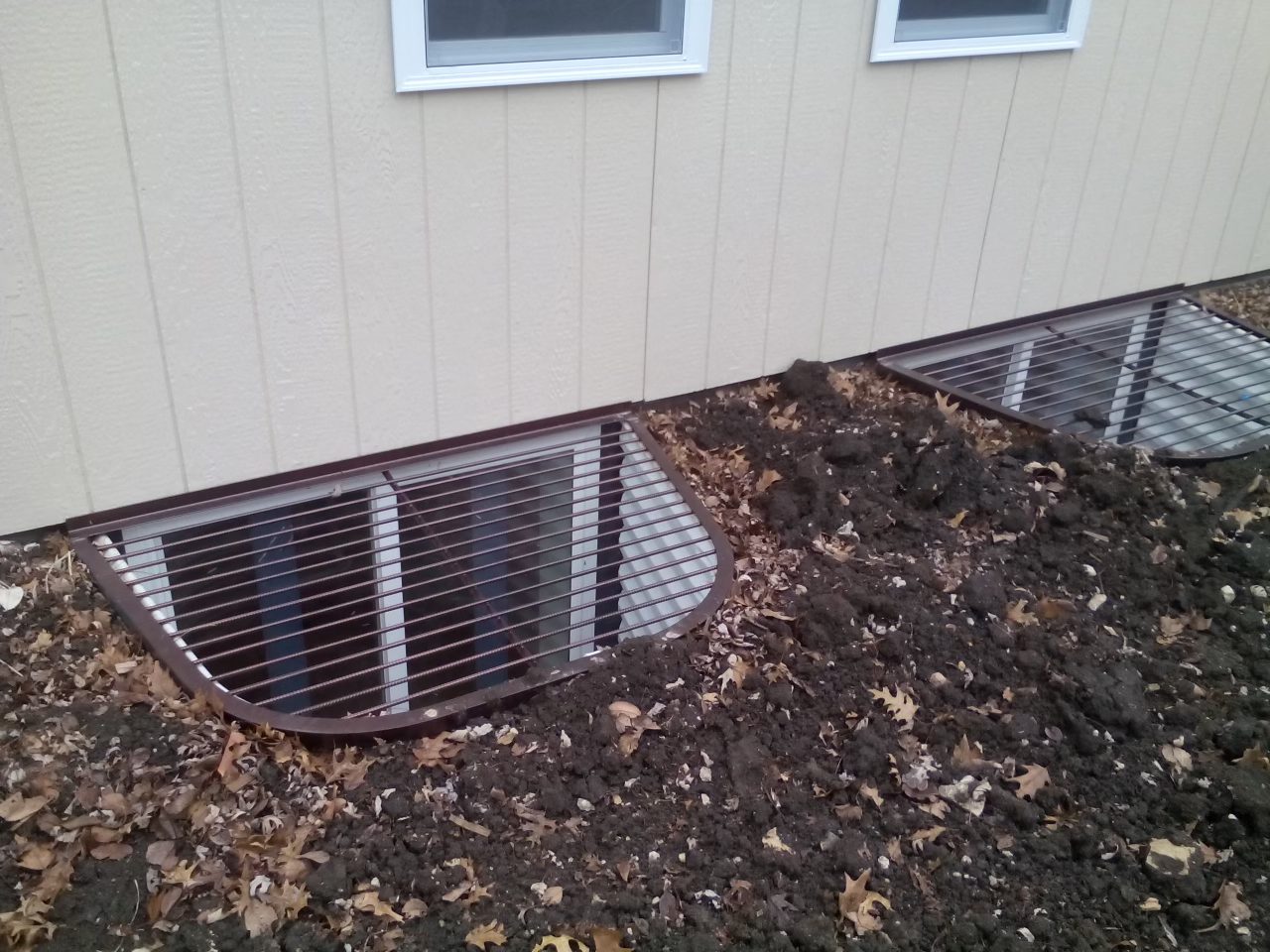 Egress window well with a metal safety grate along the outside of a house