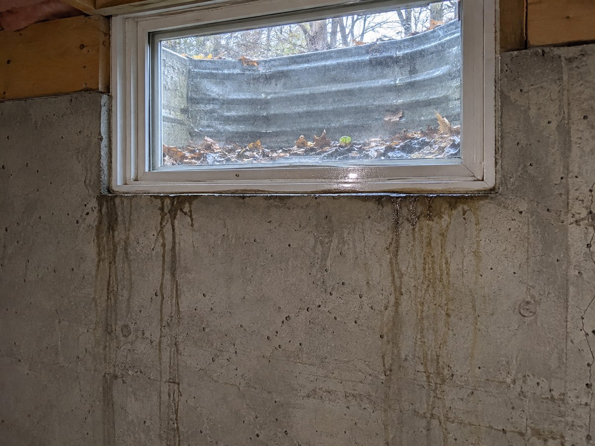 Water stain running down a basement wall below a window