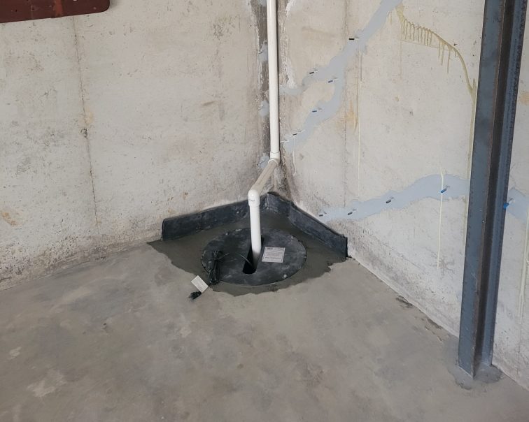 Sealed sump pump basin in a basement corner with a white discharge pipe