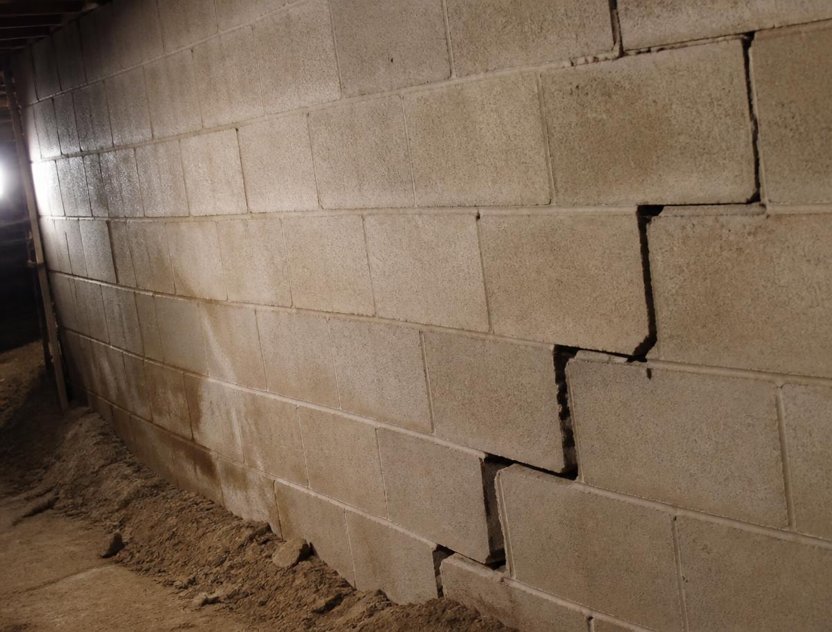 Bowing cinder block foundation wall with a stair-step crack in a basement
